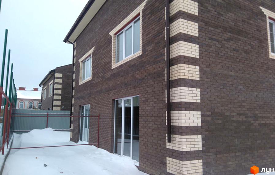 Зовнішній вигляд будинку з коричневої цегли з білими вставками. Навколо будинку засніжена територія та паркан.