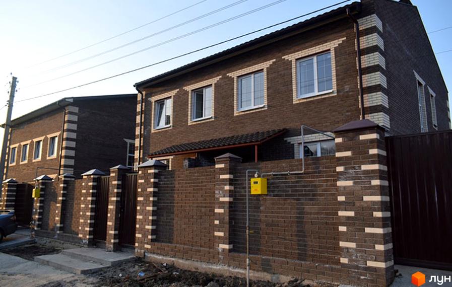 Фасад двоповерхового будинку з коричневої цегли з білими декоративними вставками. Огороджена територія цегляним парканом з колонами.