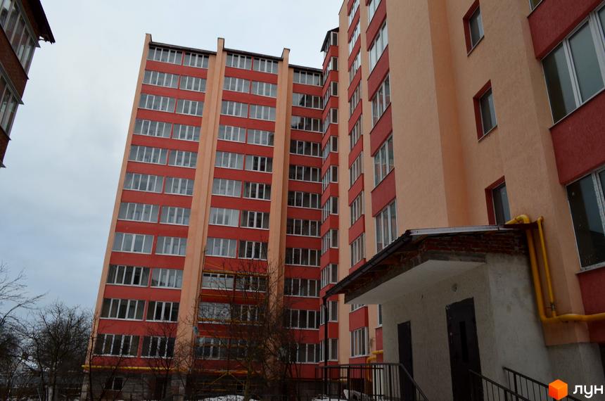 Житловий комплекс Львівська брама. Зовнішній вигляд багатоповерхових будинків з червоними та бежевими фасадами та численними вікнами. Біля будинку видно вхідну групу з навісом та жовті газові труби.