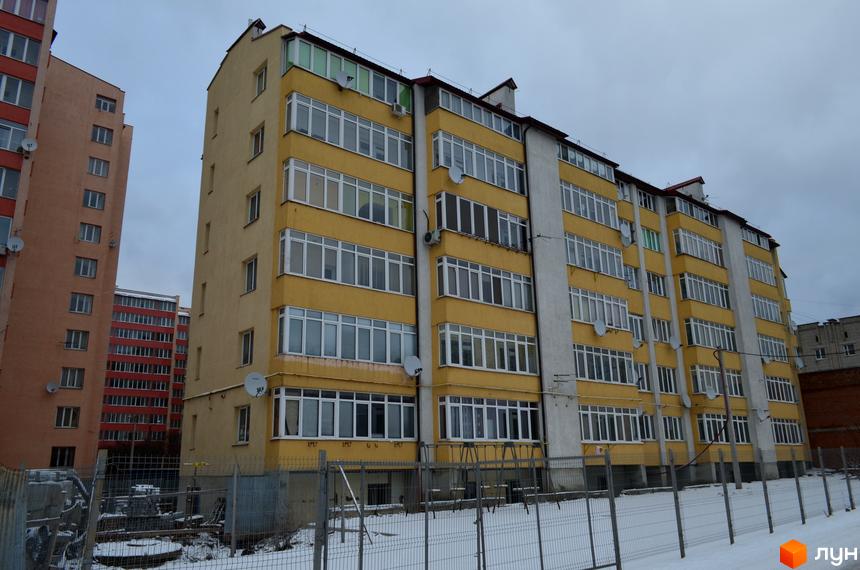Житловий комплекс Львівська брама: багатоповерховий жовтий будинок з численними балконами та вікнами. Навколо огороджена територія зі снігом та деревами.