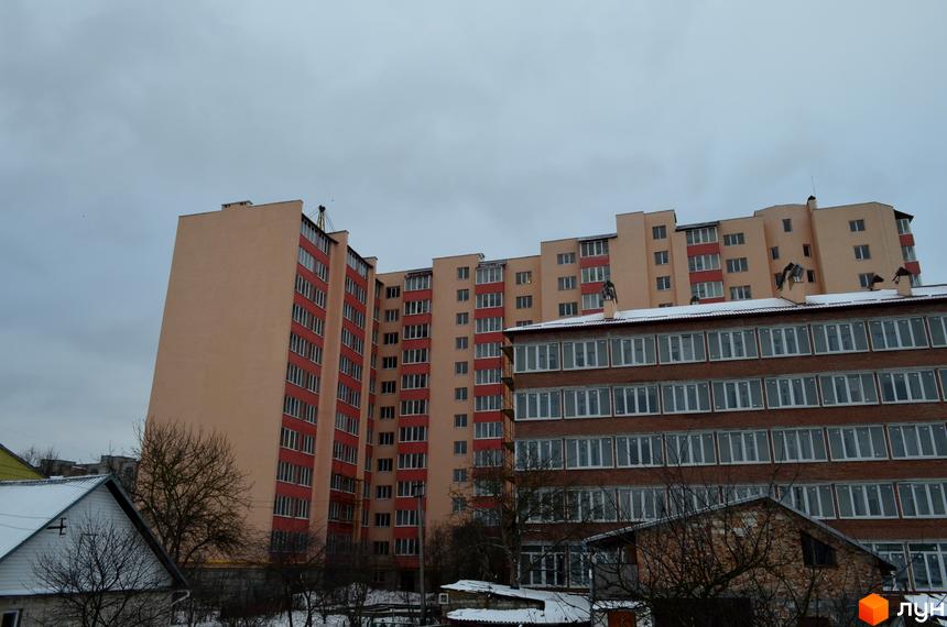 Новобудова Львівська брама з червоної цегли та бежевого кольору. Навколо новобудови видно дерева та засніжені дахи будинків.