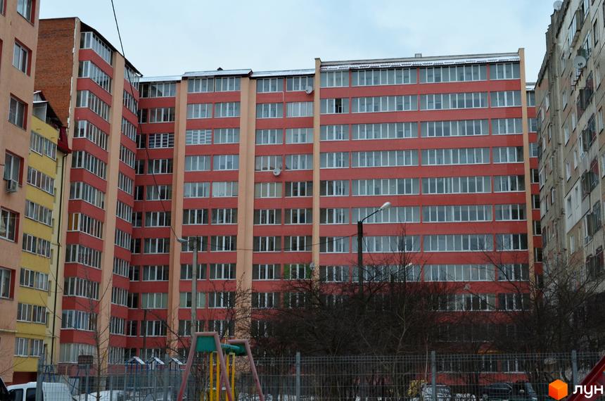 Зовнішній вигляд житлового комплексу Львівська брама з червоно-бежевими фасадами та численними вікнами. На прибудинковій території видно дитячий майданчик та паркан.