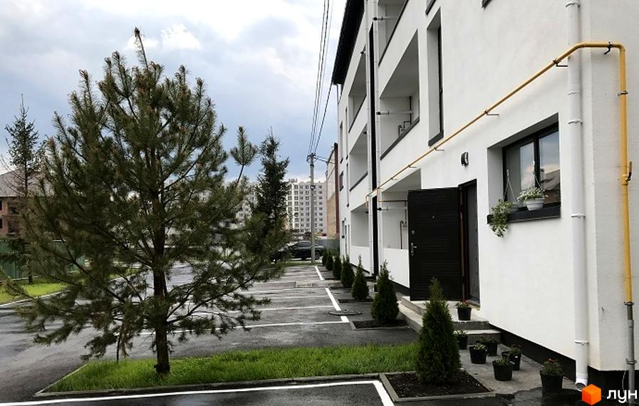 Зовнішній вигляд новобудови ЖК Нова Данія з парковкою та зеленими насадженнями. Сучасна архітектура та доглянута прибудинкова територія.