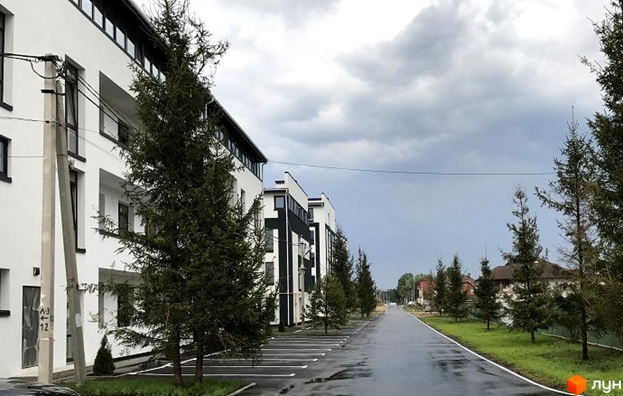 Зовнішній вигляд новобудови ЖК Нова Данія з паркуванням та деревами. Сучасний житловий комплекс з біло-чорними фасадами та доглянутою територією.