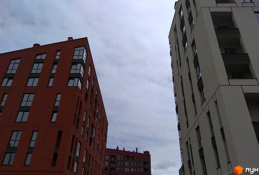 Новобудова ЖК Spectrum з червоної та білої цегли з великою кількістю вікон. Зовнішній вигляд будівель з балконами та скляними елементами.