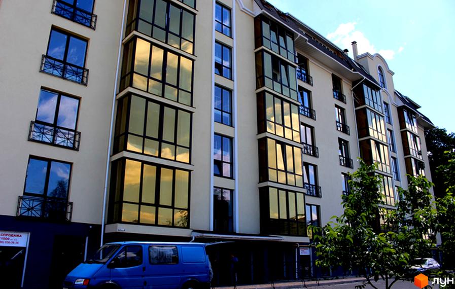 Житловий комплекс Almond apartments - фасади будівель з великими вікнами та балконами, відображають хмари. Поруч припаркований синій фургон.