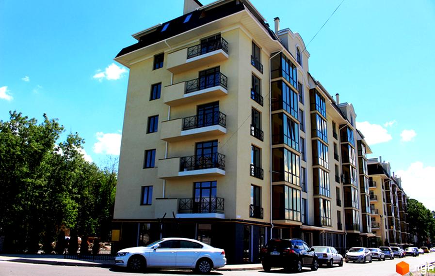 Житловий комплекс Almond apartments – це сучасна новобудова з елегантними балконами та великими вікнами. Перед будинком розташована вулиця з припаркованими автомобілями.