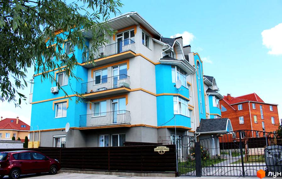 Багатоповерховий будинок з блакитними та сірими фасадами. На території є парковка та ковані ворота.