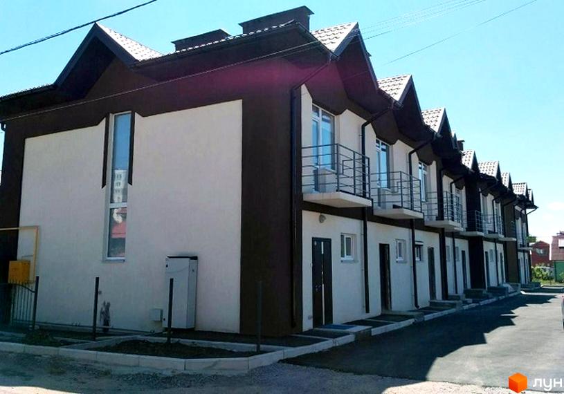 Зовнішній вигляд таунхаусів СанЛенд з коричневими та білими фасадами, балконами та дахами. Прибудинкова територія з доріжками та зеленими насадженнями.