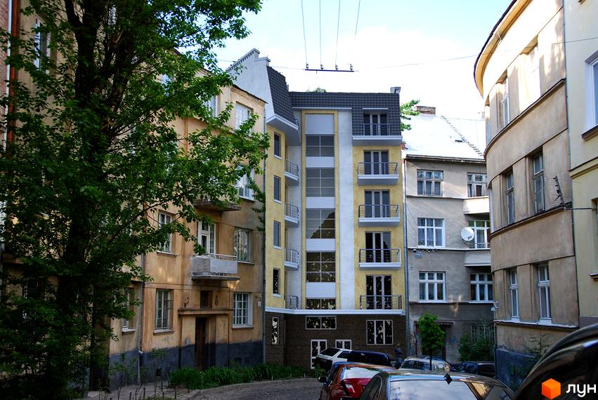 Новобудова на вул. Тарнавського, 48. Фасад будівлі виконаний у жовтих та білих тонах з елементами сірого. Балкони мають металеві огорожі. Навколо будинку зелені насадження та припарковані автомобілі.