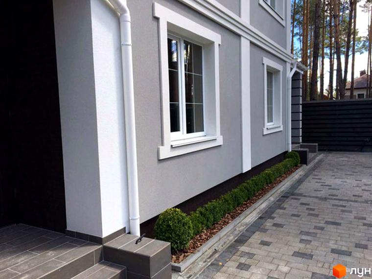 Зовнішній вигляд таунхауса Pacific Park. Сірий фасад будівлі з білими віконними рамами та декоративними елементами. На прибудинковій території бруківка та зелені насадження.