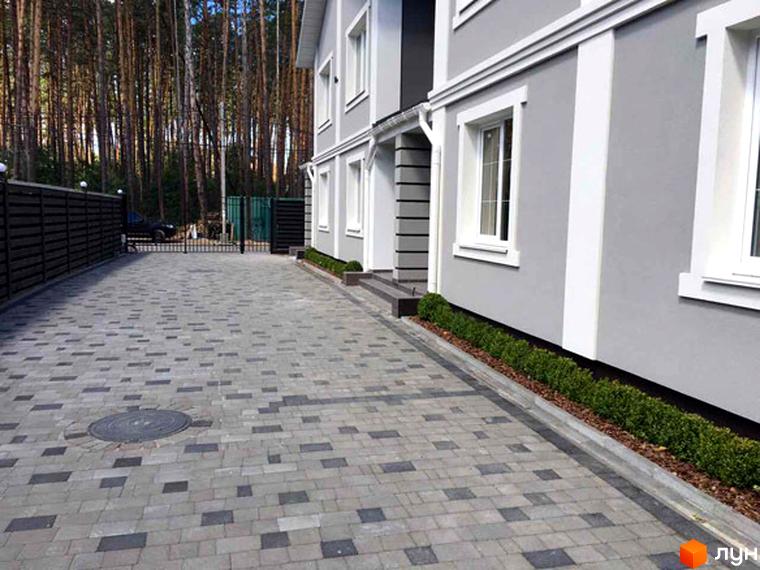 Фасад будинку в ЖК Pacific Park з сірою штукатуркою та білими віконними рамами. Бруківка на подвір'ї та зелені насадження вздовж будинку.