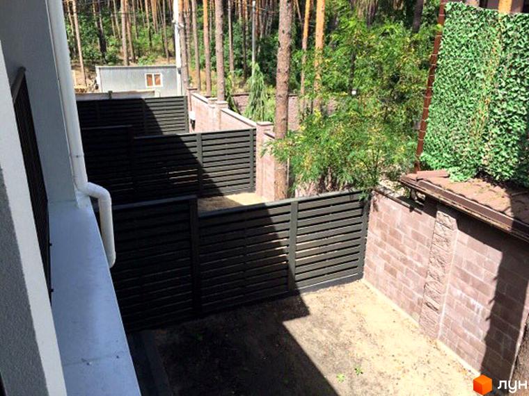 Зовнішній вигляд таунхауса Pacific Park з білим водостоком, огородженою прибудинковою територією з темними парканами, цегляною стіною та зеленою огорожею.