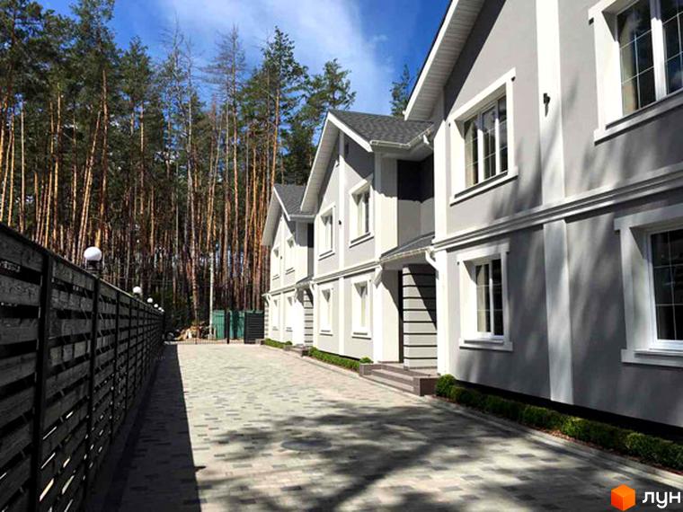 Таунхаус Pacific Park: фасади сірих будинків з білими елементами, доріжка з бруківки та зелені насадження. Збоку видно огорожу та ліс.