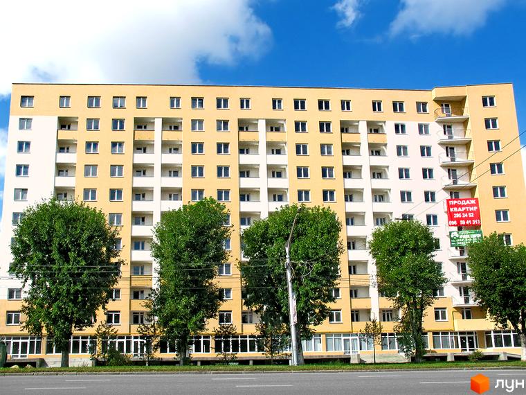 Зовнішній вигляд багатоповерхового житлового комплексу на Стрийській, 204, з жовтим фасадом та білими вставками. Навколо будівлі зелені дерева та дорога.