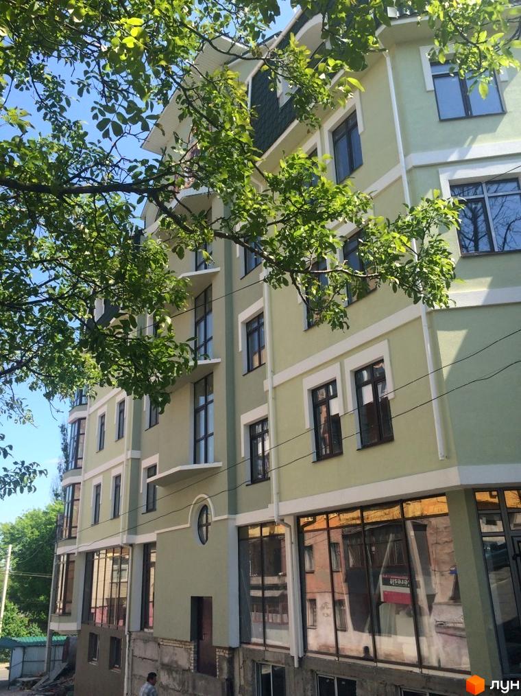 Фасад новобудови на вул. Монастирська (Володарського) з зеленим оздобленням та великими вікнами. Навколо будівлі видно дерева та блакитне небо.