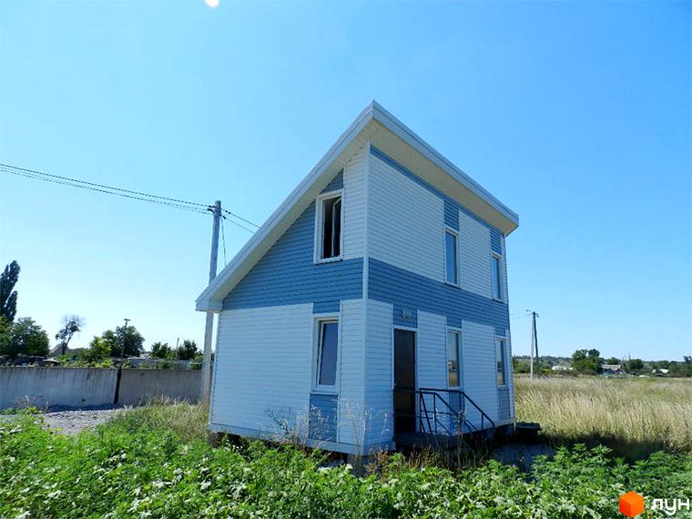 Двоповерховий будинок з блакитно-білим фасадом у Котеджному містечку Созидатель Хаус. Навколо будинку зелена трава та дерева під чистим блакитним небом.