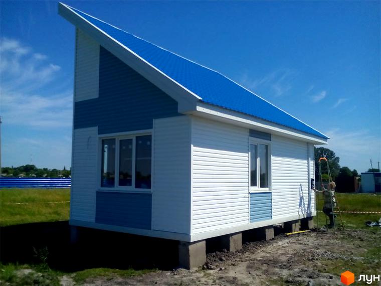 Котеджне містечко КМ Созидатель Хаус: одноповерховий будинок з біло-блакитним фасадом та синім дахом на бетонному фундаменті. Навколо будинку зелена трава та невисокі дерева.