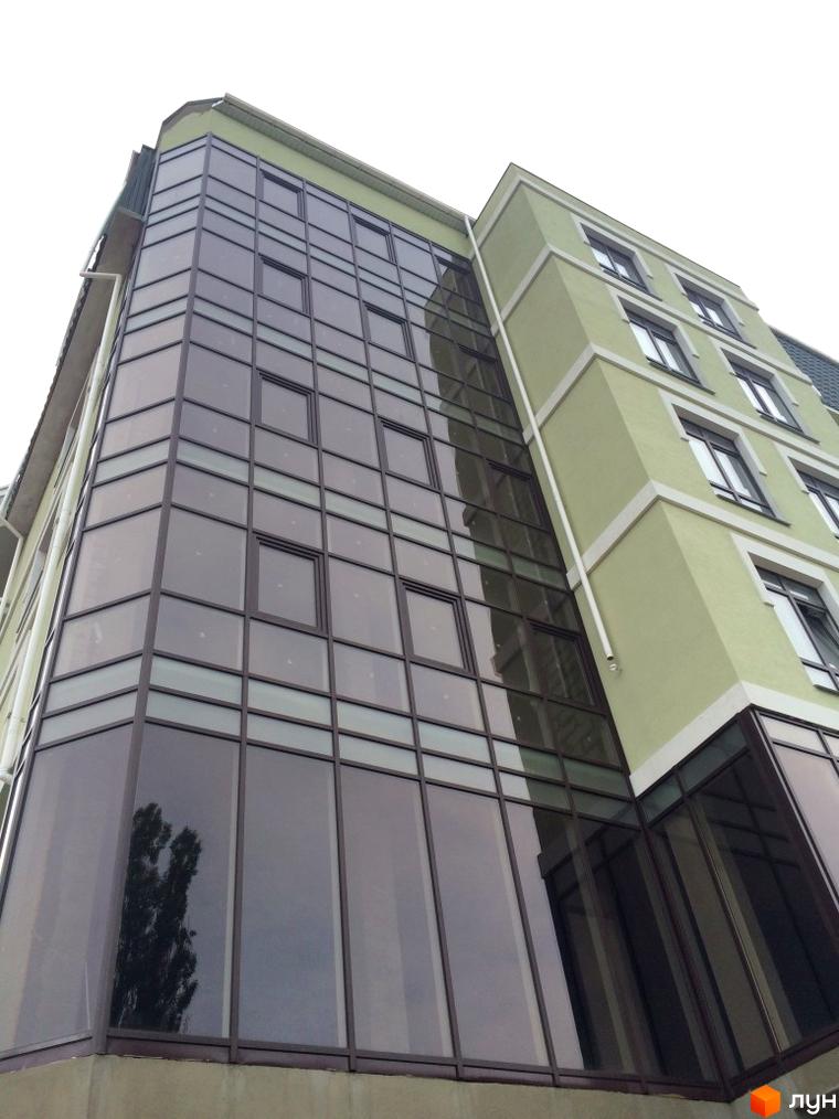 Фасад житлового комплексу на вулиці Монастирська (Володарського) з панорамним склінням та світло-зеленими стінами. Зовнішній вигляд будівлі з низького ракурсу.