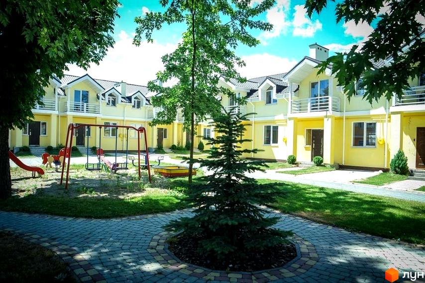 Вигляд Котеджного містечка Sun City з дитячим майданчиком на прибудинковій території. Двоповерхові будинки з мансардами та зеленим газоном.