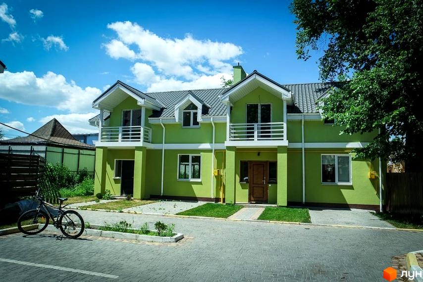 Зображення двоповерхового будинку в Котеджному містечку Sun City. Перед будинком викладена тротуарна плитка та стоїть велосипед.