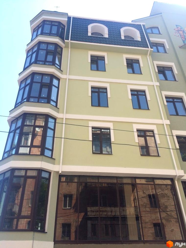 Фасад новобудови на вул. Монастирська (Володарського) з еркерними вікнами та панорамним склінням першого поверху. Будинок має світло-зелене оздоблення стін та темний дах.