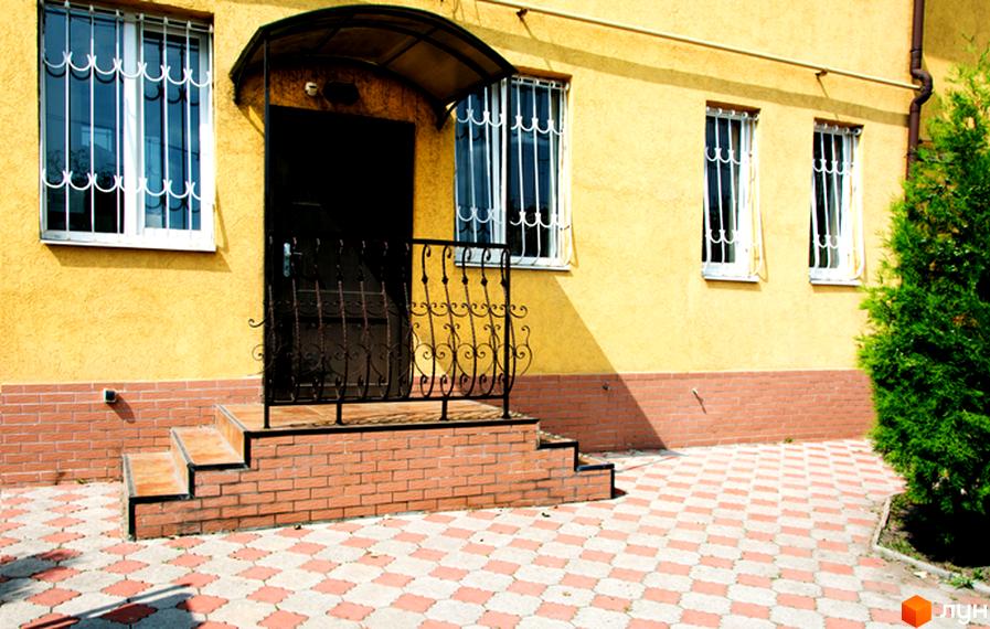 Sanhouse: жовтий будинок з вікнами під решітками та цегляними сходами веде до плитки на подвір'ї.