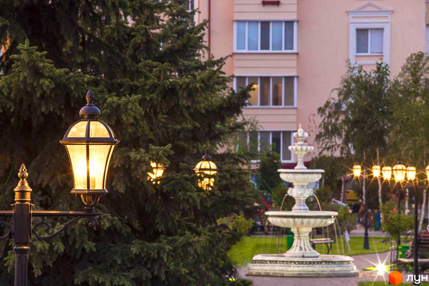 Житловий комплекс Львівський: фасади будинків та паркова зона з фонтаном та ліхтарями. Вечірній вид на новобудову з підсвіченими ліхтарями та зеленою зоною.