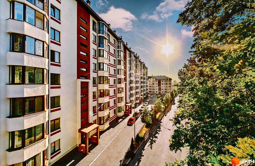 Зовнішній вигляд будинку ЖК Празький квартал з фасадами білого та червоного кольору. Прибудинкова територія з дорогою та деревами.