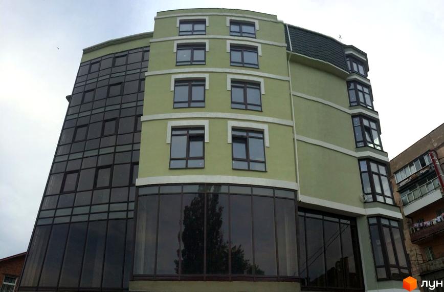 Фасад новобудови на вулиці Монастирська (Володарського) з панорамним склінням та світло-зеленими стінами. Будинок має багатоповерхову структуру з виступаючими елементами та темним дахом.