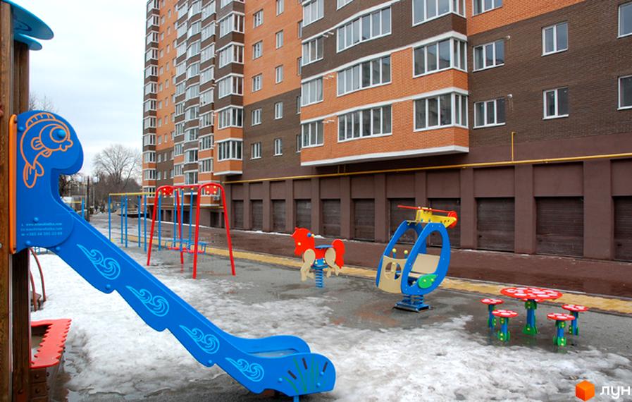 Житловий комплекс Капучіно з багатоповерховими цегляними фасадами. На прибудинковій території облаштовано дитячий майданчик.