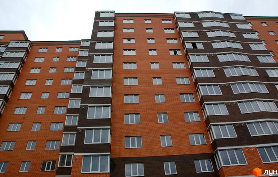 Зовнішній вигляд новобудови ЖК Капучіно з цегляним фасадом та великою кількістю вікон. Багатоквартирний будинок з балконами та лоджіями.