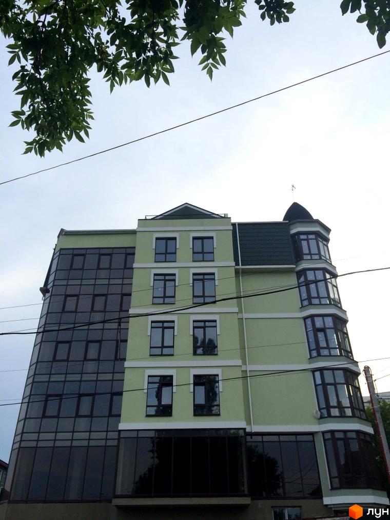 Зовнішній вигляд новобудови на вулиці Монастирській (Володарського) з панорамними вікнами та балконами. Зелена фасадна частина будівлі контрастує з темними вікнами.