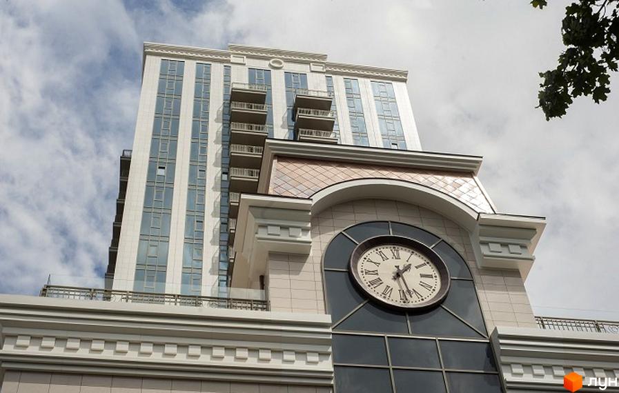 Житловий комплекс Арт Холл з годинником на фасаді та балконами. Прибудинкова територія озеленена деревами та рослинами.