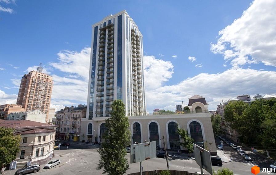 Клубний будинок „Арт Холл“ – висотна новобудова з балконами та скляними фасадами. Навколо будівлі розташована міська вулиця з автомобілями та деревами.