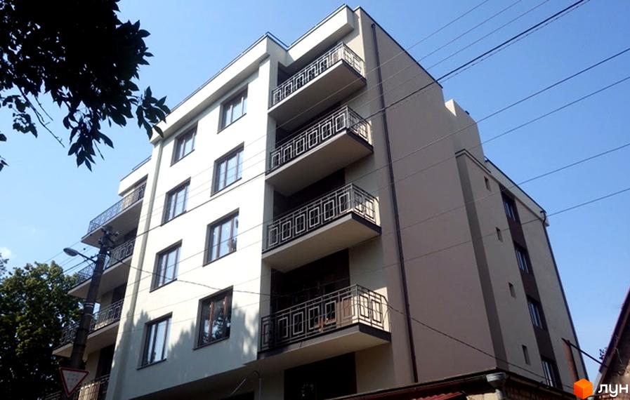 Зображення фасаду багатоповерхового будинку. На фасаді будинку розташовані балкони з кованими огорожами. Небо блакитне, сонячна погода.