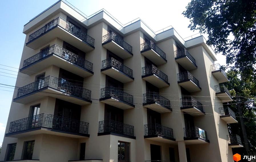 Клубний будинок Brownie House: багатоквартирний будинок світлого кольору з балконами, прикрашеними темними металевими поручнями. Навколо видно зелені дерева.