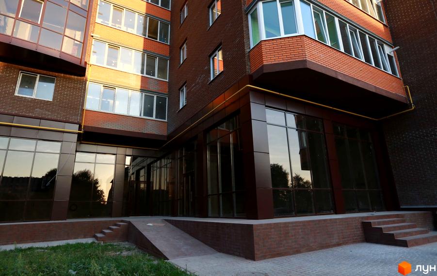 Житловий комплекс Галицький Лев: багатоповерховий будинок з цегляними стінами та великими вікнами. На першому поверсі комерційні приміщення, поруч пандус та сходи.