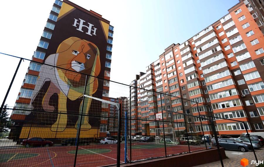 Житловий комплекс Галицький Лев: багатоповерхова будівля з великим муралом лева на фасаді. Поруч огороджений спортивний майданчик.