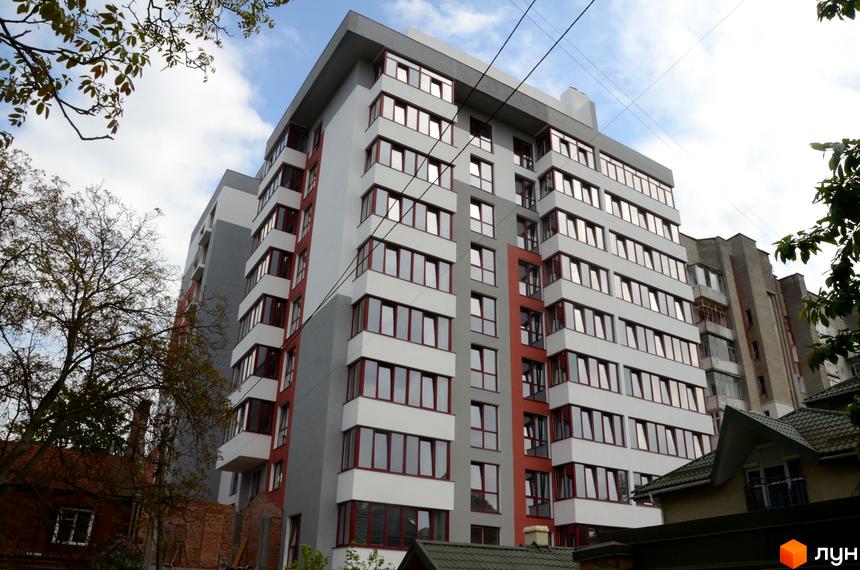 Багатоповерховий житловий комплекс Panorama з сіро-білим фасадом та червоними віконними рамами. Територія навколо включає зелені насадження та сусідні споруди.