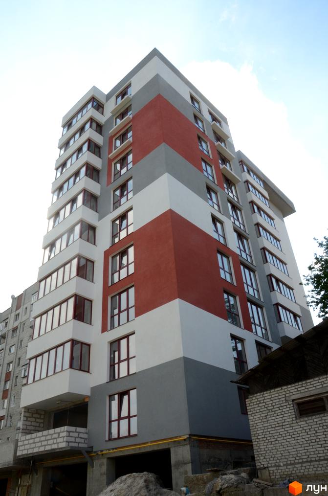 Новобудова Panorama: багатоповерховий будинок з фасадом білого, сірого та червоного кольорів. На передньому плані видно будівельний майданчик.