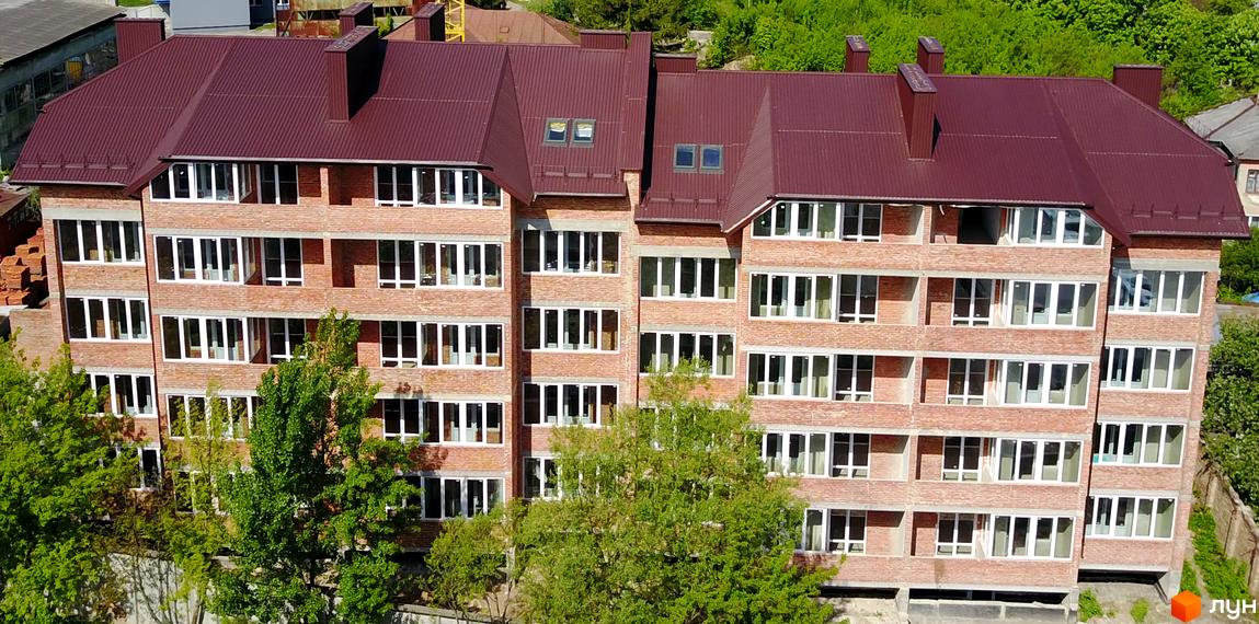 Зовнішній вигляд новобудови на вул. Кармелюка, 12. Цегляний будинок з коричневим дахом та численними вікнами. Навколо ростуть дерева.