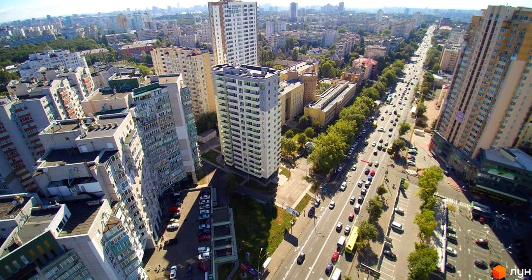 Вид на житловий комплекс на проспекті Валерія Лобановського, 15/7. Багатоповерхові будинки з фасадами світлих кольорів, розташовані вздовж широкої вулиці з автомобілями та деревами.