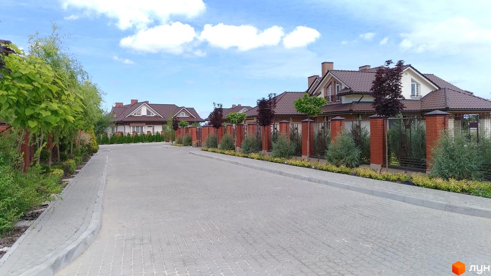 Котеджне містечко Панська Гора: затишна вулиця з цегляними будинками та доглянутими зеленими насадженнями. Сучасний житловий комплекс з акуратними фасадами та огорожею.