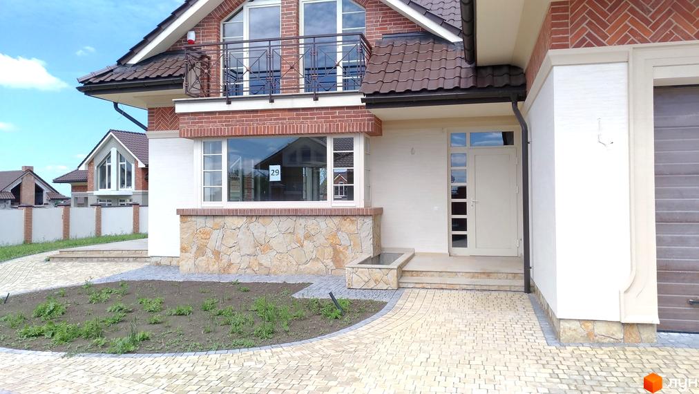 Котеджне містечко Панська Гора: фасад будинку з цегляним оздобленням та великими вікнами. Прибудинкова територія з бруківки та зеленими насадженнями.