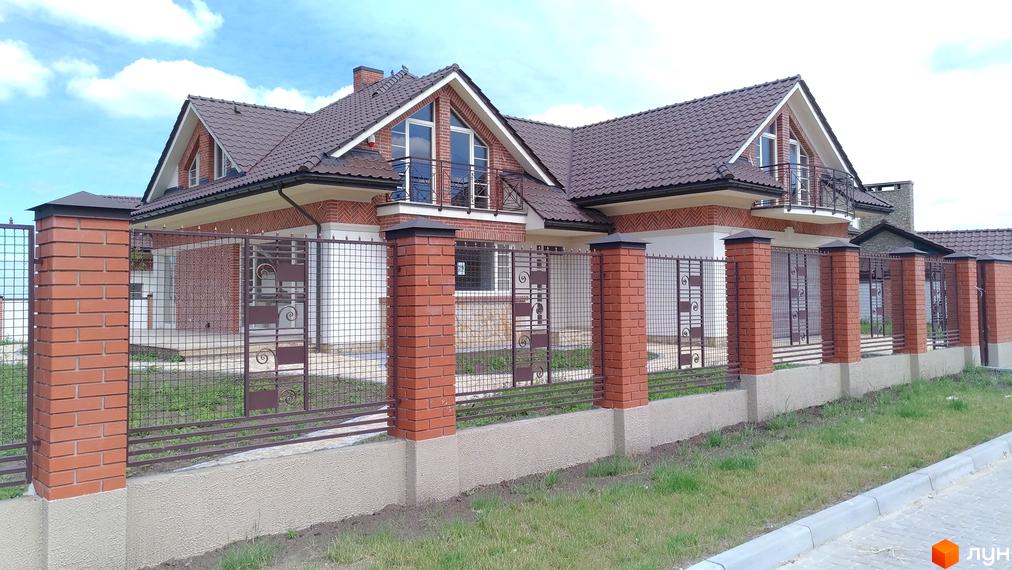 Котеджне містечко КМ Панська Гора. Зовнішній вигляд будинку з цегляними колонами та металевою огорожею. Прибудинкова територія з газоном та тротуаром.