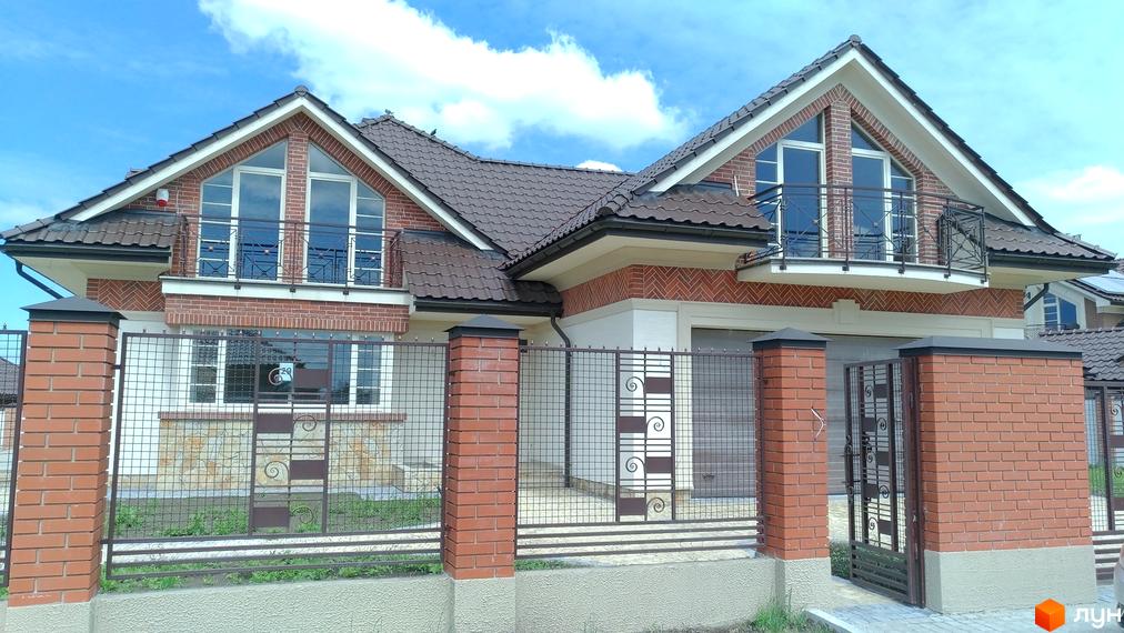 Котеджне містечко КМ Панська Гора. Зовнішній вигляд будинку з червоної цегли з балконами та коричневим дахом. Огороджена територія з кованими елементами.