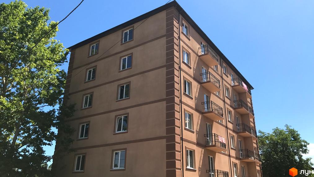 Зовнішній вигляд будинку ЖК Адмірал з балконами та вікнами на фоні блакитного неба. Поруч видно зелене дерево.