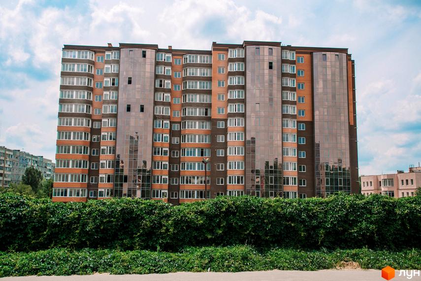 Зображення багатоповерхового будинку з великими вікнами. Житловий комплекс Олександрівський 1 на фоні зелених насаджень.