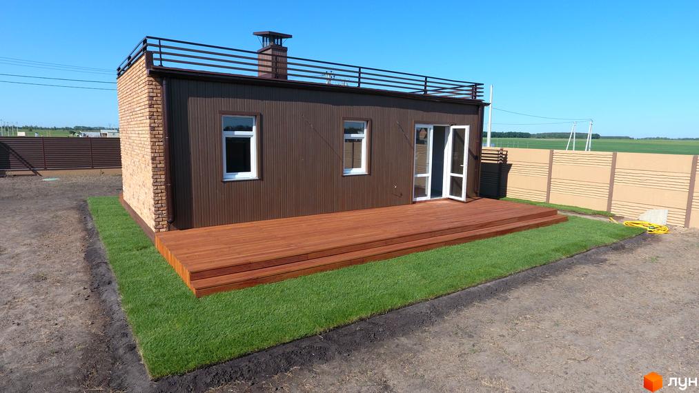 Зображення будинку в Котеджному кварталі „Фортеця Колонщини“. Одноповерховий будинок з терасою та газоном на прибудинковій території.